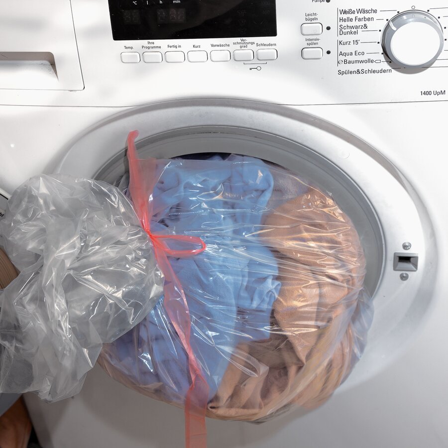 Beutel wird geschlossen mit Inhalt in die Wäschetrommel gegeben Beutel wird geschlossen mit Inhalt in die Wäschetrommel gegeben